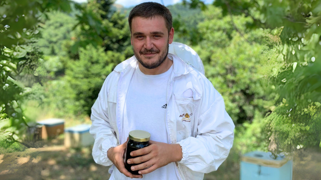 Beekeeper Thomas at his hives holding a jar of honey