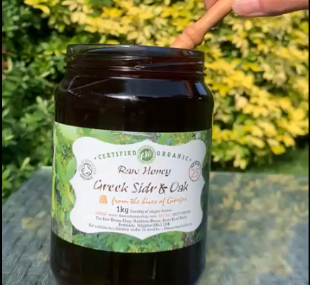 Jar of dark brown honey in a glass jar with the lid off and a honey dipper in the jar