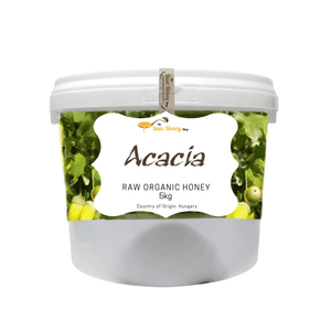 A 5kg plastic tub of Acacia Raw Organic Honey by The Raw Honey, Shop featuring a white lid, a white label with green acacia leaves, set against a plain white background.