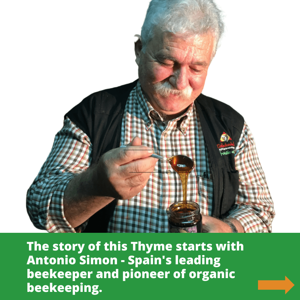Spanish beekeeper Antonio Simon smiling looking at a spoonful of dark honey dripping into glass honey jar