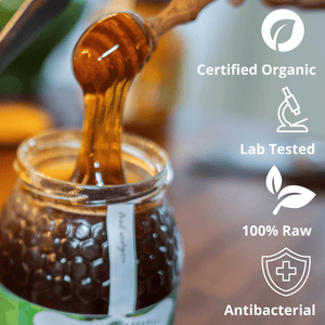 A close-up of honey dripping from a wooden honey dipper into a glass jar of raw honey, with text overlays on the right reading 'Certified Organic', 'Lab Tested', '100% Raw', and 'Antibacterial'.