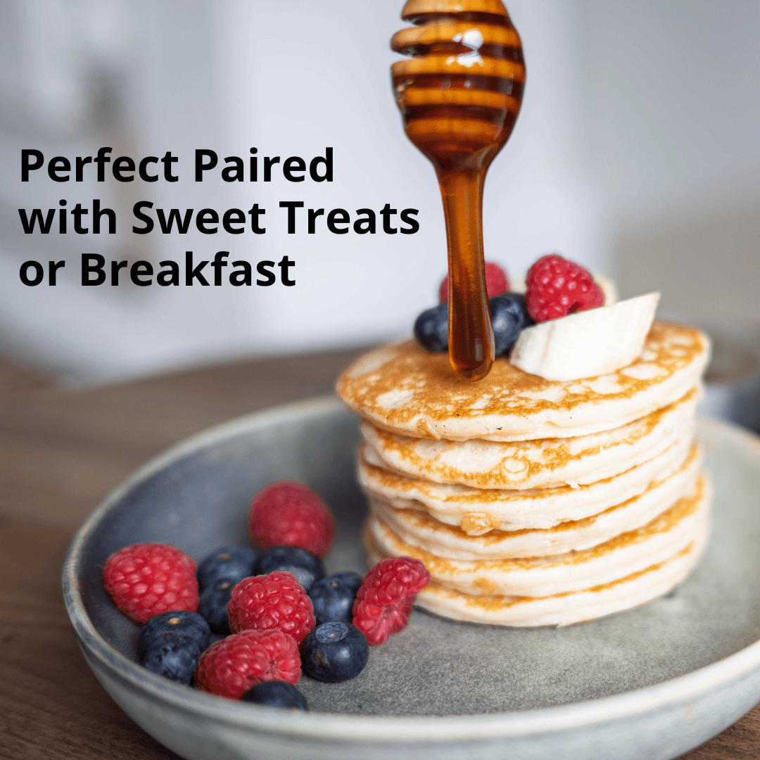 A stack of golden pancakes topped with a drizzle of honey, a wooden honey dipper, and fresh berries on a gray plate, with the text 'Perfect Paired with Sweet Treats or Breakfast' on the left.