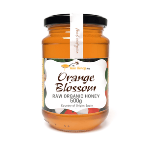 A 500g glass jar of 'Antonios Raw Organic Orange Blossom' honey by 'The Honey Shop' with a black lid and a white label, set against a plain white background.