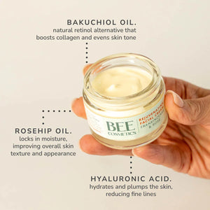 A hand holding a small glass jar of Bee Cosmetics Rejuvenating Facial Cream with text callouts describing its ingredients: bakuchiol oil, rosehip oil, and hyaluronic acid. 