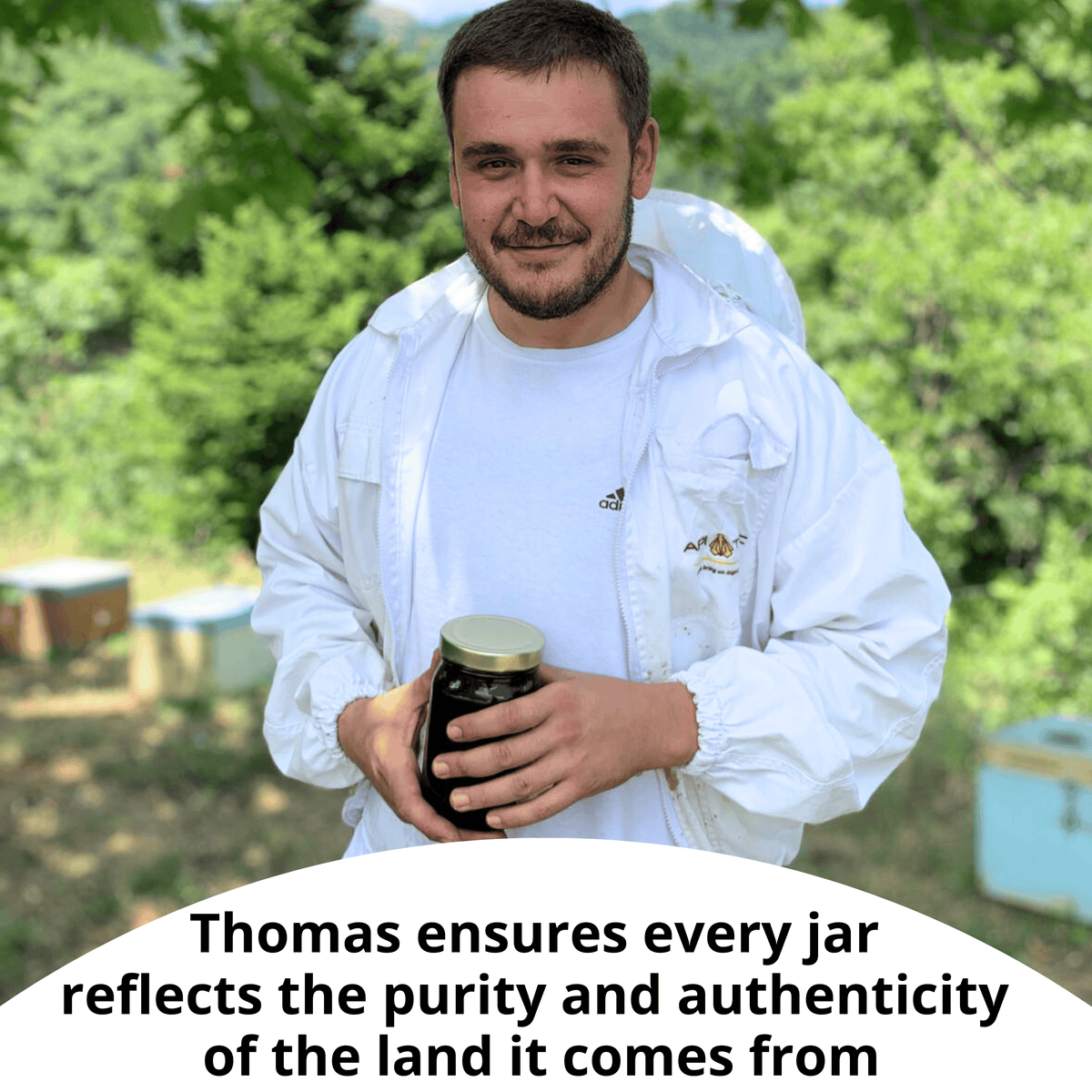 A man in a white beekeeping jacket stands outdoors holding a glass jar with a gold lid, with beehives and green trees in the background. A white text overlay at the bottom reads, 'Thomas ensures every jar reflects the purity and authenticity of the land it comes from'.