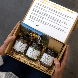 Box of honey jars with a person holding it, featuring a scenic photo and text on the lid.