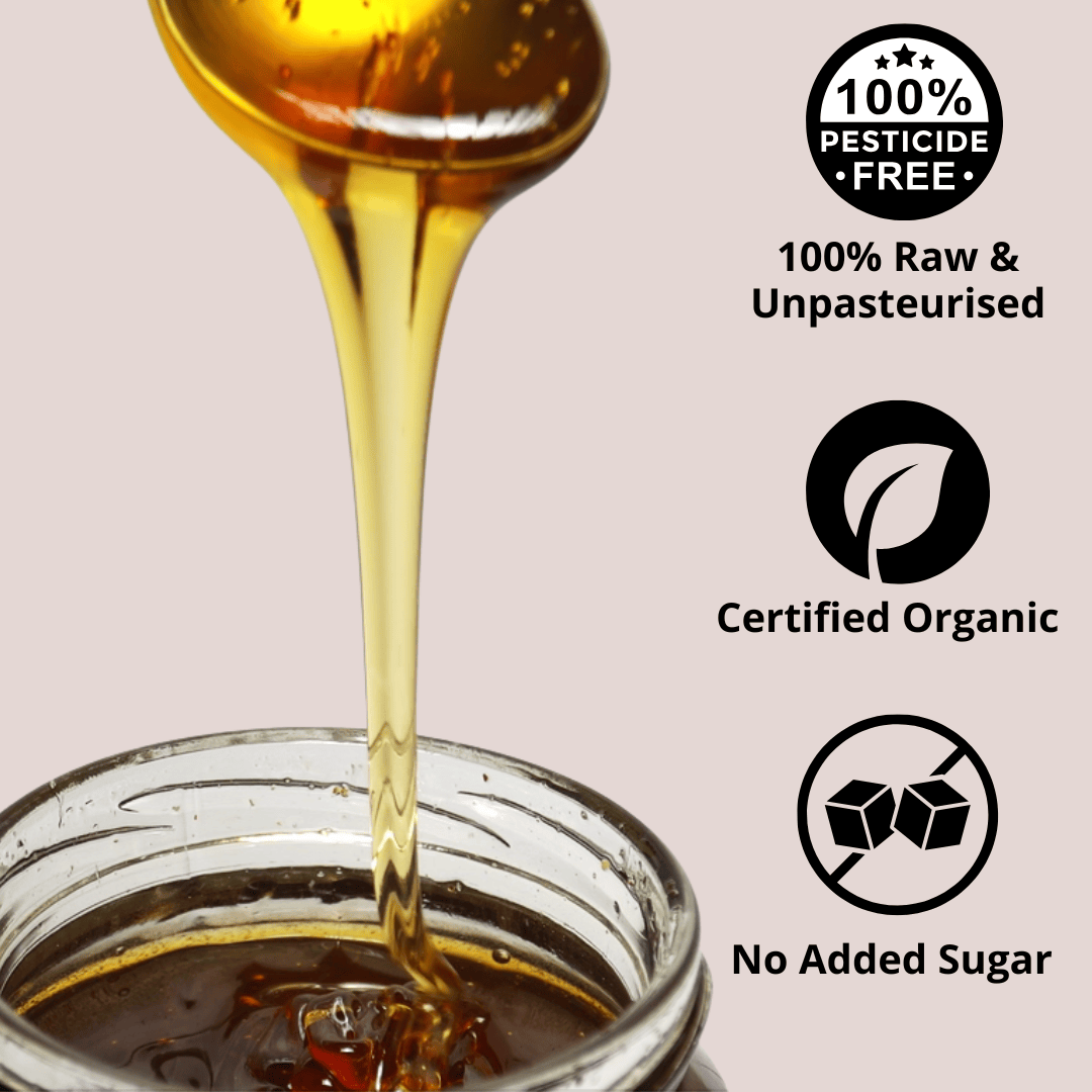 A close-up of golden honey dripping from a spoon into a glass jar, with text callouts on a pale pink background reading '100% Pesticide Free,' '100% Raw & Unpasteurised,' 'Certified Organic,' and 'No Added Sugar.'.