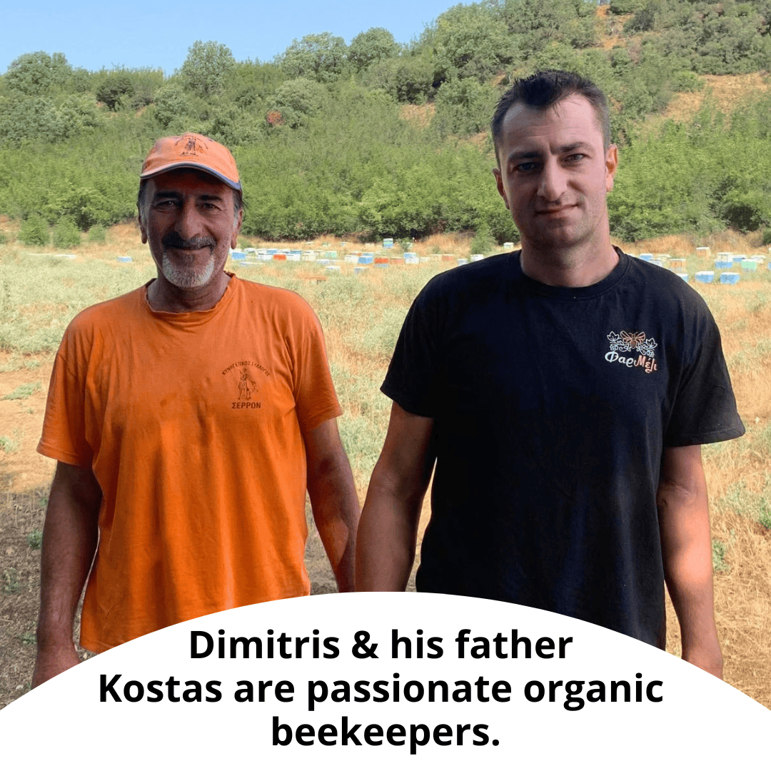 Two men standing outdoors in a field with beehives in the background. One man wears an orange t-shirt and cap, and the other wears a black t-shirt with a bee logo.