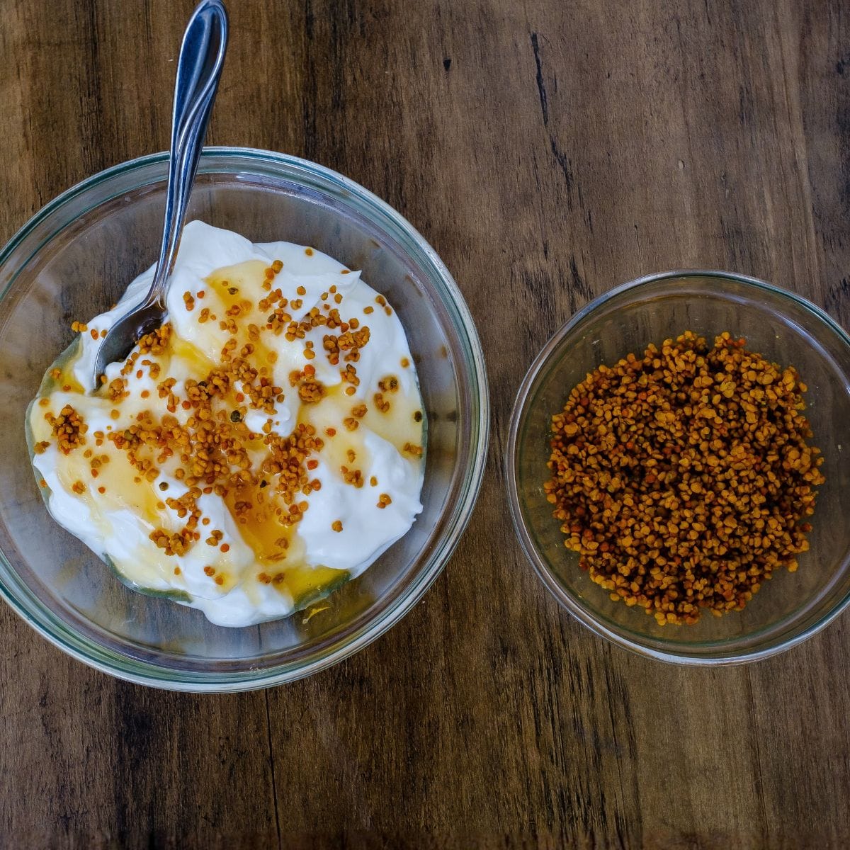 Bowl of yogurt with honey and a small bowl of bee pollen on a wooden surface