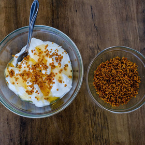 Bowl of yogurt with honey and a small bowl of bee pollen on a wooden surface