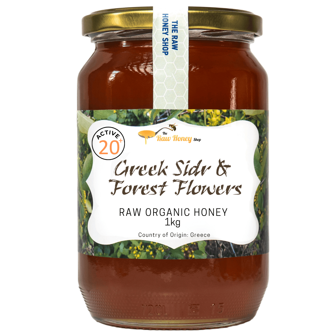 A 1kg glass jar of Greek Sidr & Forest Flowers Raw Organic Honey by The Raw Honey Shop, featuring a gold metal lid and a white label with green and yellow accents, set against a plain white background.
