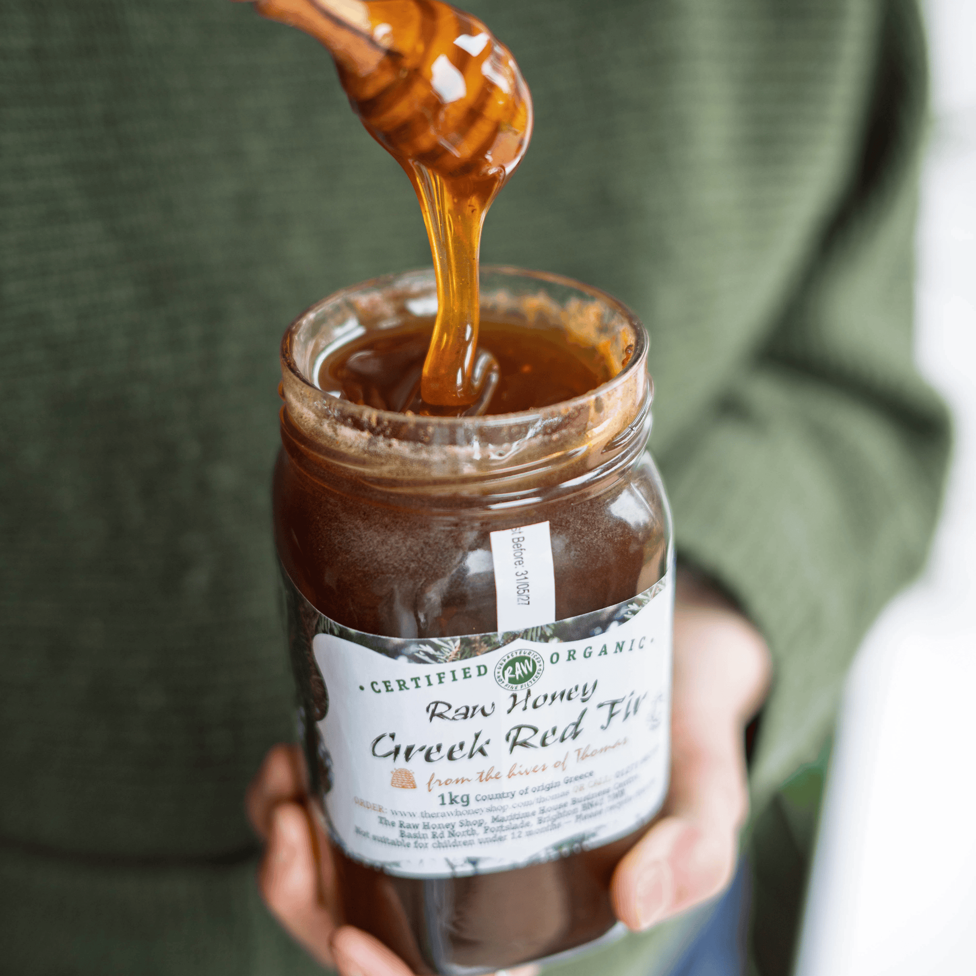 Jar of honey with a honey dipper, held by a person wearing a green sweater.