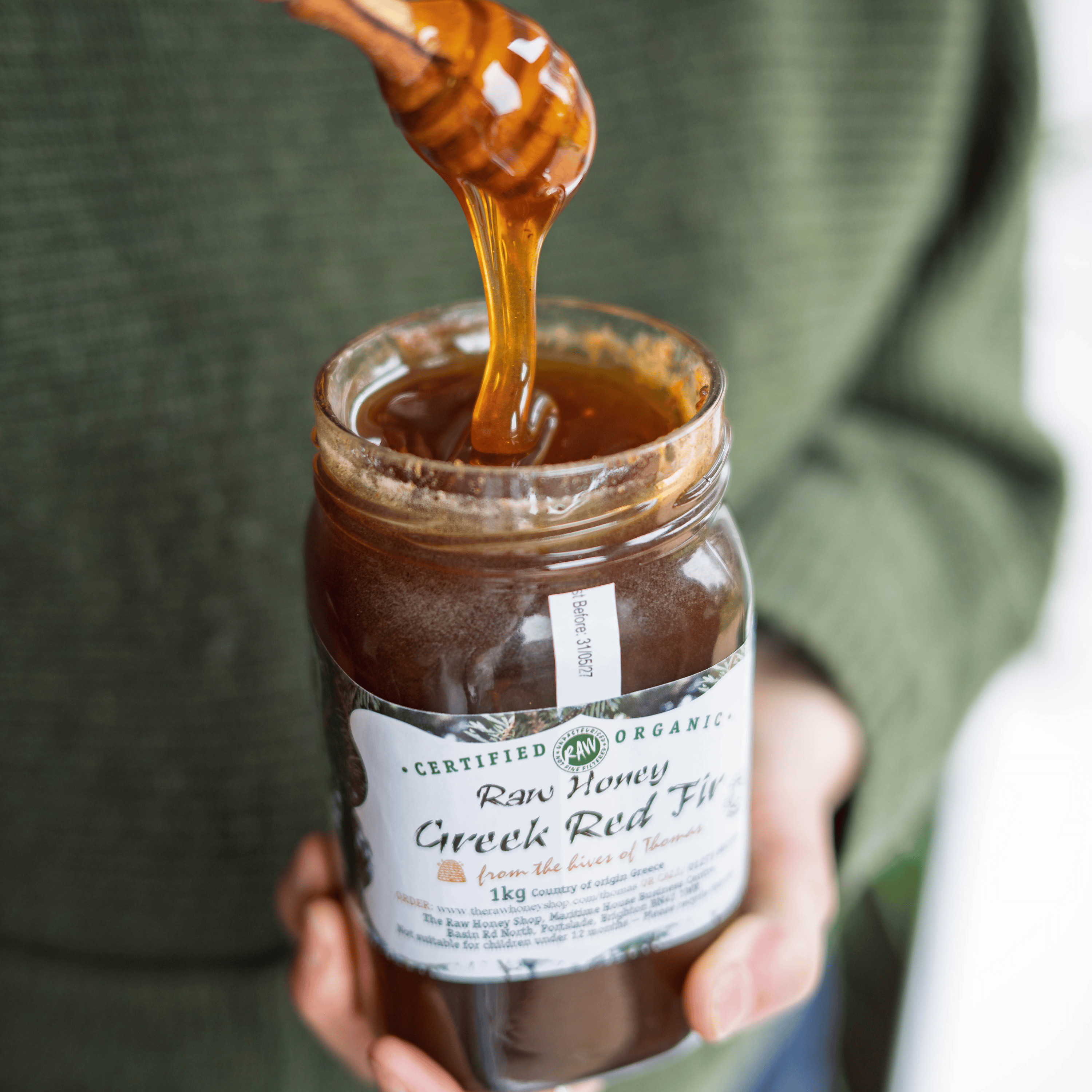 Jar of honey with a honey dipper, held by a person wearing a green sweater.