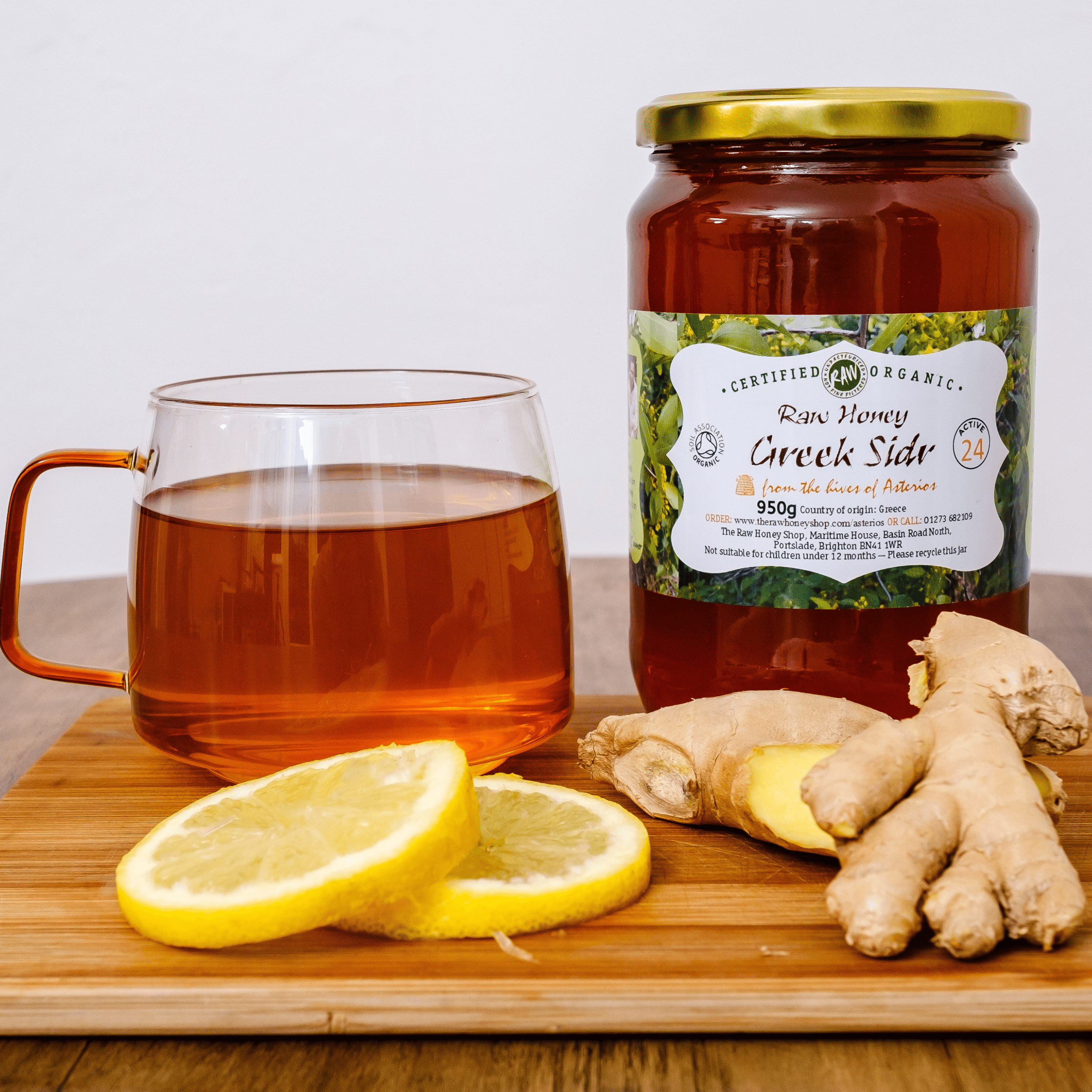 Jar of honey, glass of tea, lemon slices, and ginger on a wooden board.