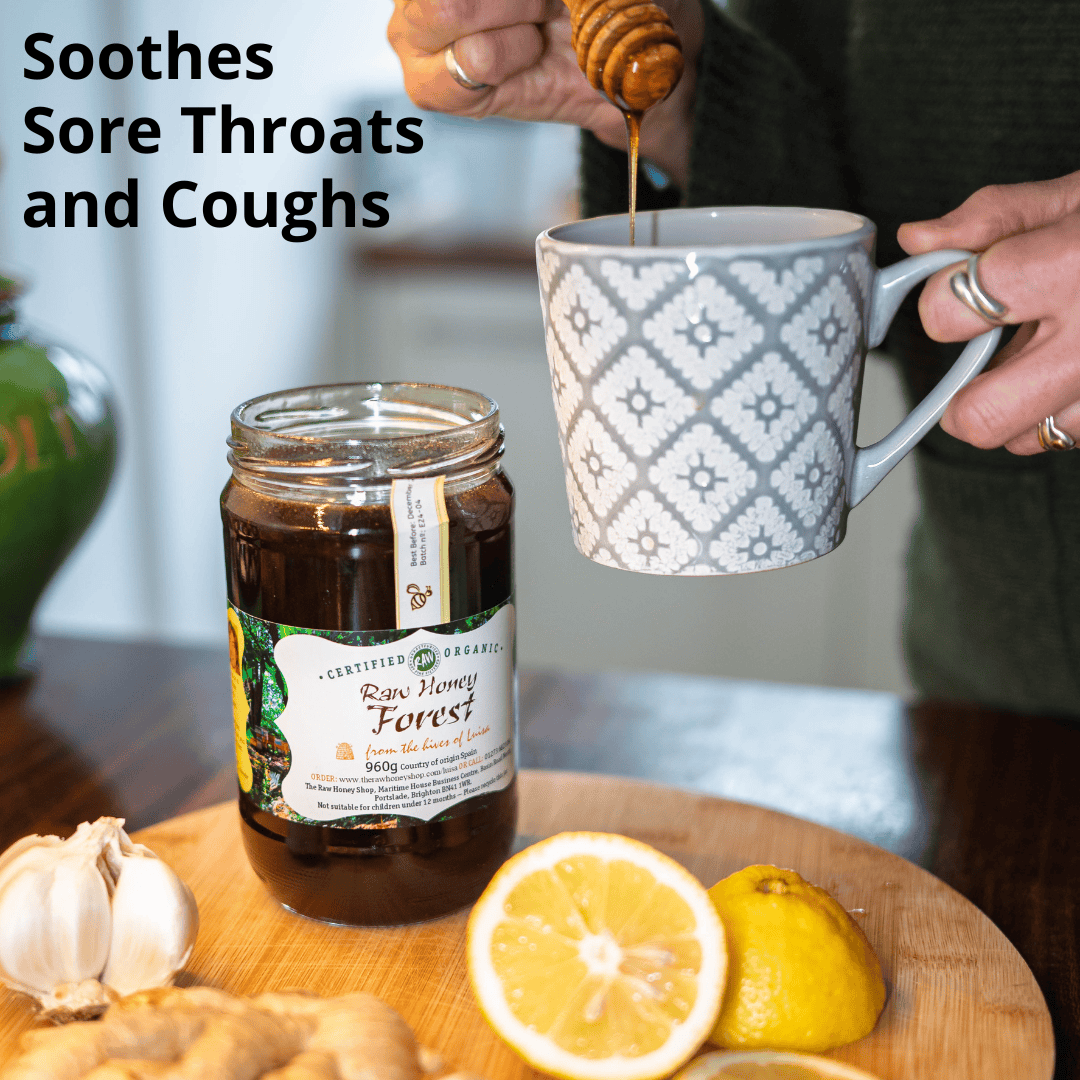 A jar of Certified Organic Raw Honey Forest honey sits on a wooden board with a lemon half, ginger, and garlic, while a person pours honey from a wooden dipper into a gray patterned mug. Text on the image reads 'Soothes Sore Throat and Coughs'.