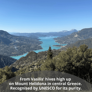Scenic landscape view of a turquoise lake winding through mountainous terrain under a clear blue sky, with a text overlay at the bottom reading, 'From Vasilis' hives high up on Mount Helidona in central Greece. Recognised by UNESCO for its purity.