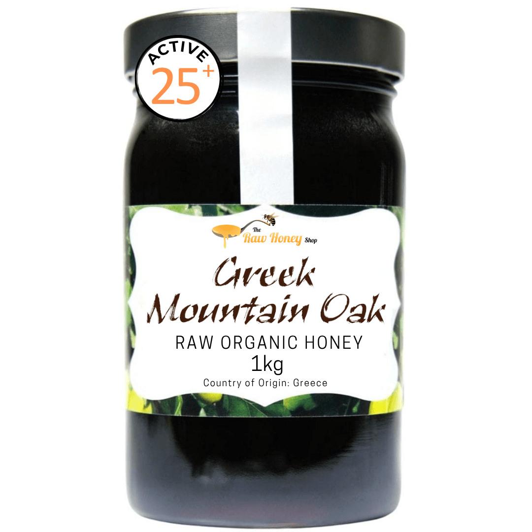 A 1kg jar of raw organic Greek Mountain Oak honey from 'The Raw Honey Shop' on a white background, featuring a black lid and a white label with green leaf graphics.