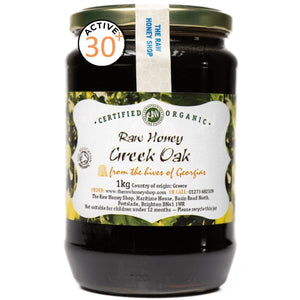 Jar of raw honey labeled 'Certified Organic Raw Honey Greek Oak' on a white background