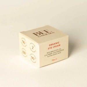 A square cream-colored cosmetic box for BEE COSMETICS Organic Eye Cream, featuring brown and red text, photographed on a matching light beige textured background.