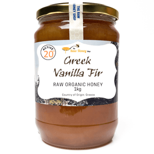 A 1kg glass jar of Active 20 Greek Vanilla Fir Raw Organic Honey on a white background, featuring a white label with brown text and a gold metal lid.
