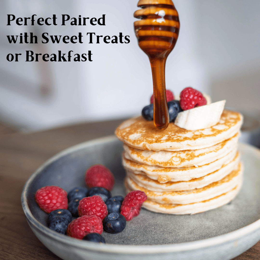 A stack of golden pancakes topped with a drizzle of honey, a wooden honey dipper, and fresh berries on a gray plate, with the text 'Perfect Paired with Sweet Treats or Breakfast' on the left.