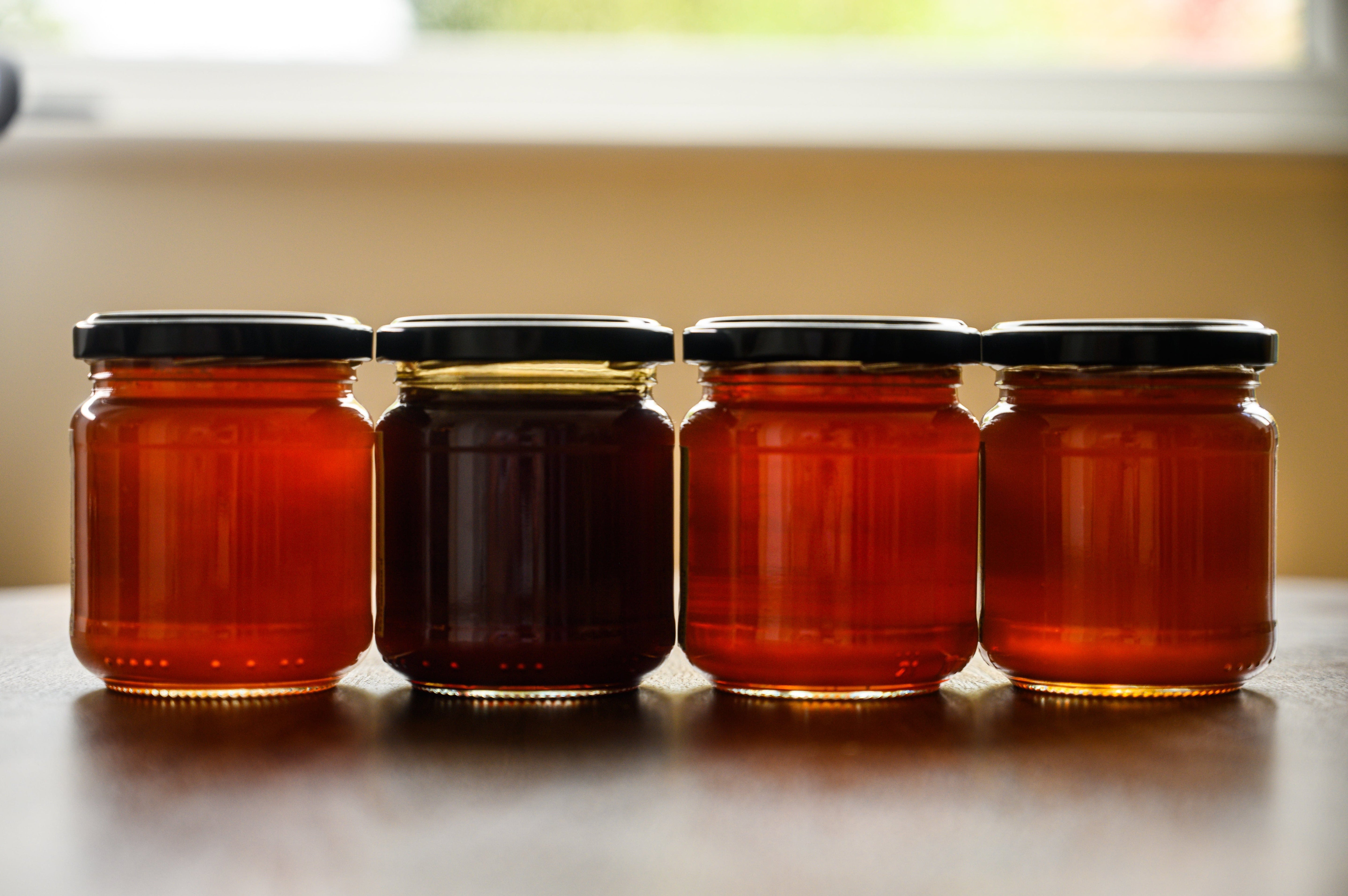 Four jars of honey lined up on a surface with a window in the background