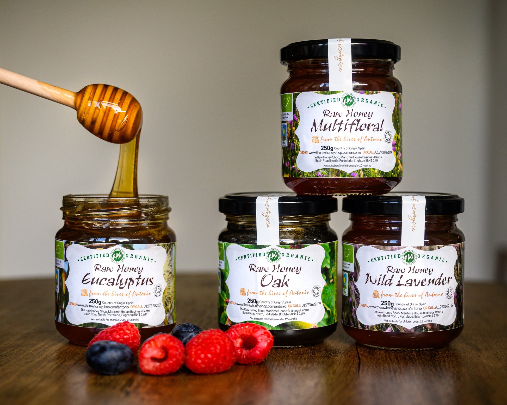 Jars of honey with labels and a honey dipper on a wooden surface.
