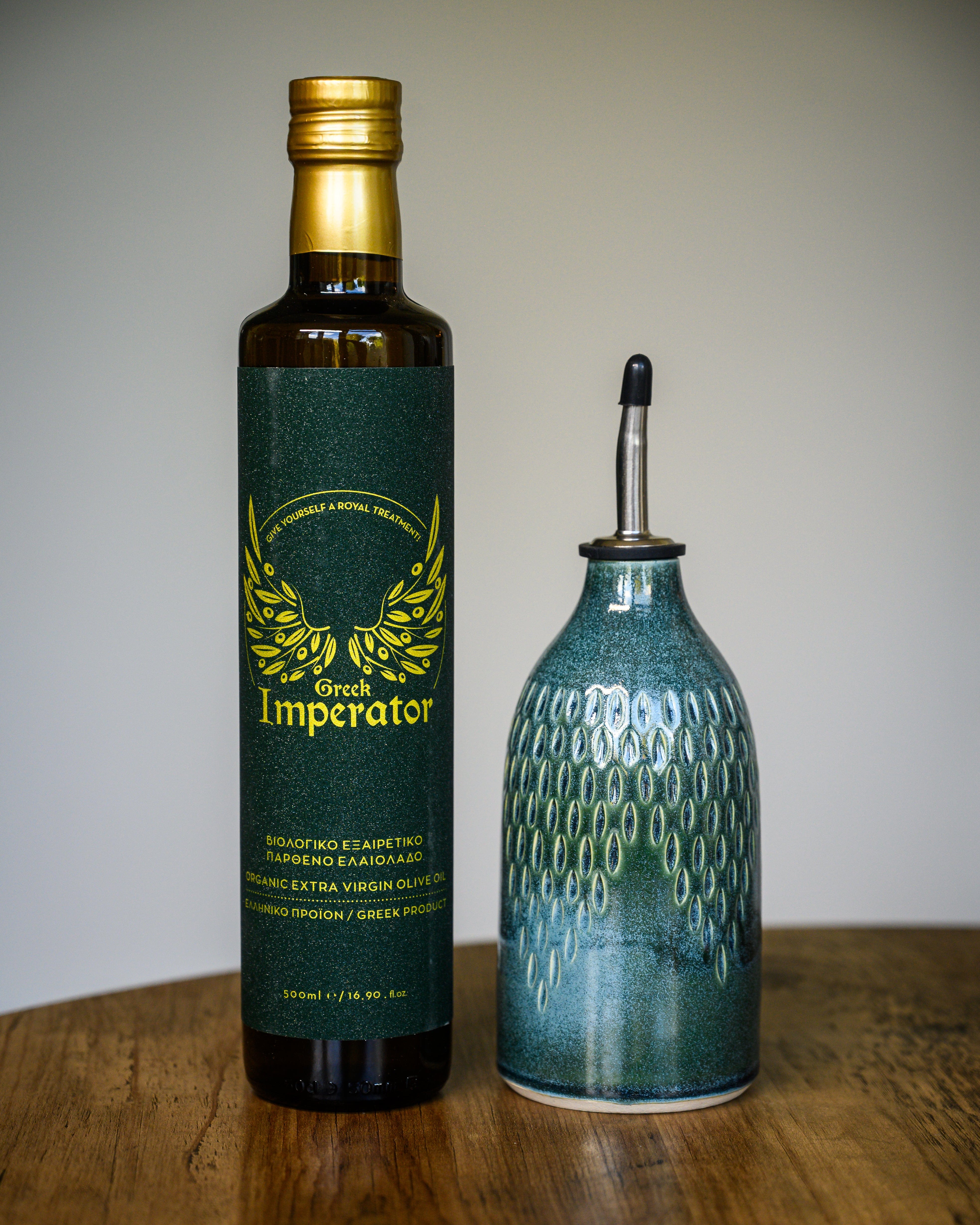 Bottle of olive oil, one green label and one ceramic, on a wooden surface.