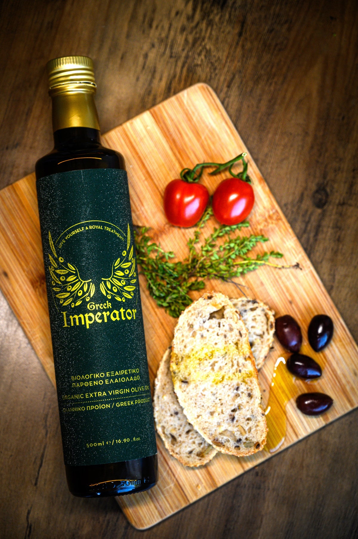 Bottle of Greek Imperator olive oil on a wooden cutting board with bread and vegetables.
