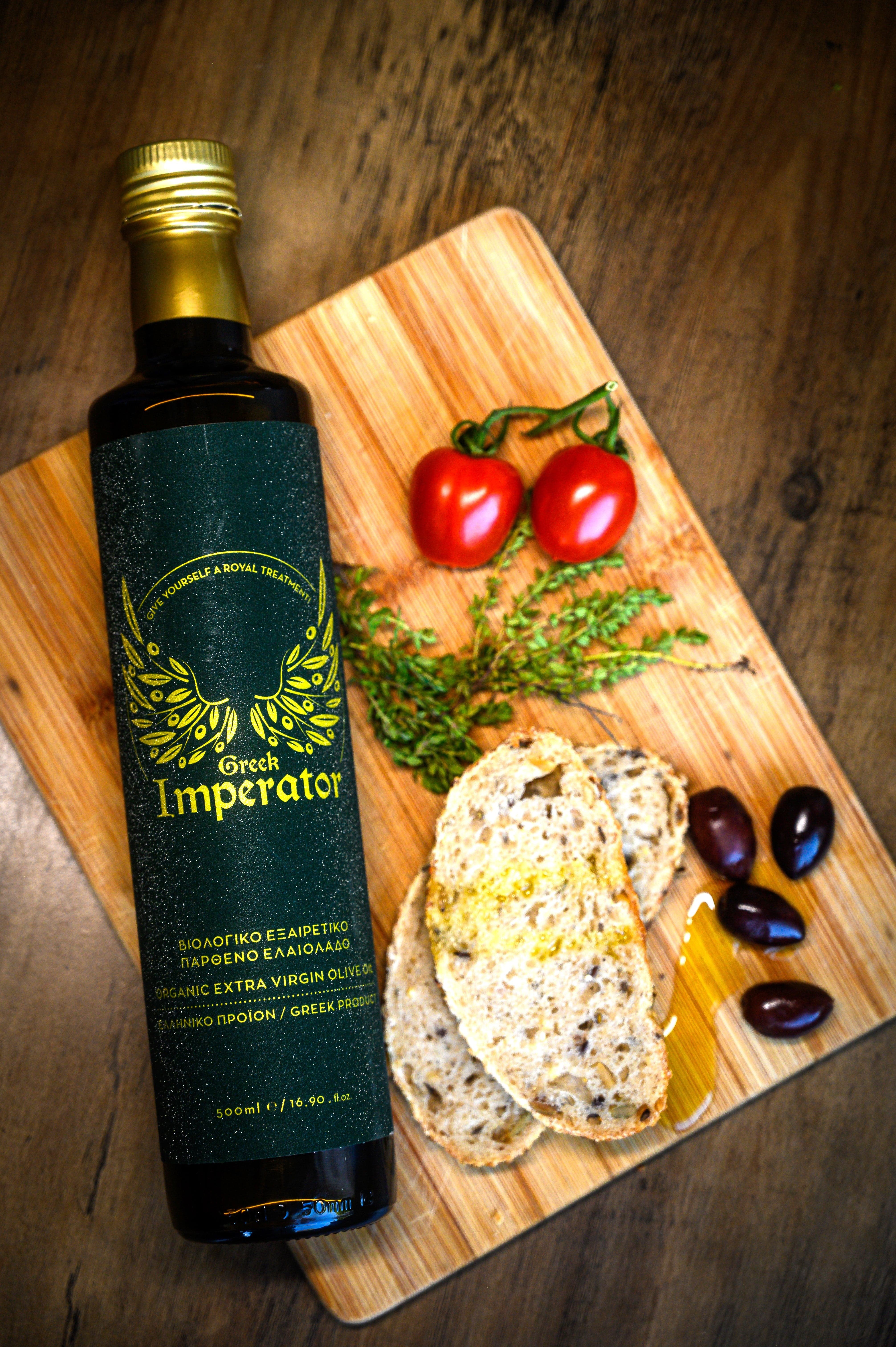 Bottle of Greek Imperator olive oil on a wooden cutting board with bread and vegetables.