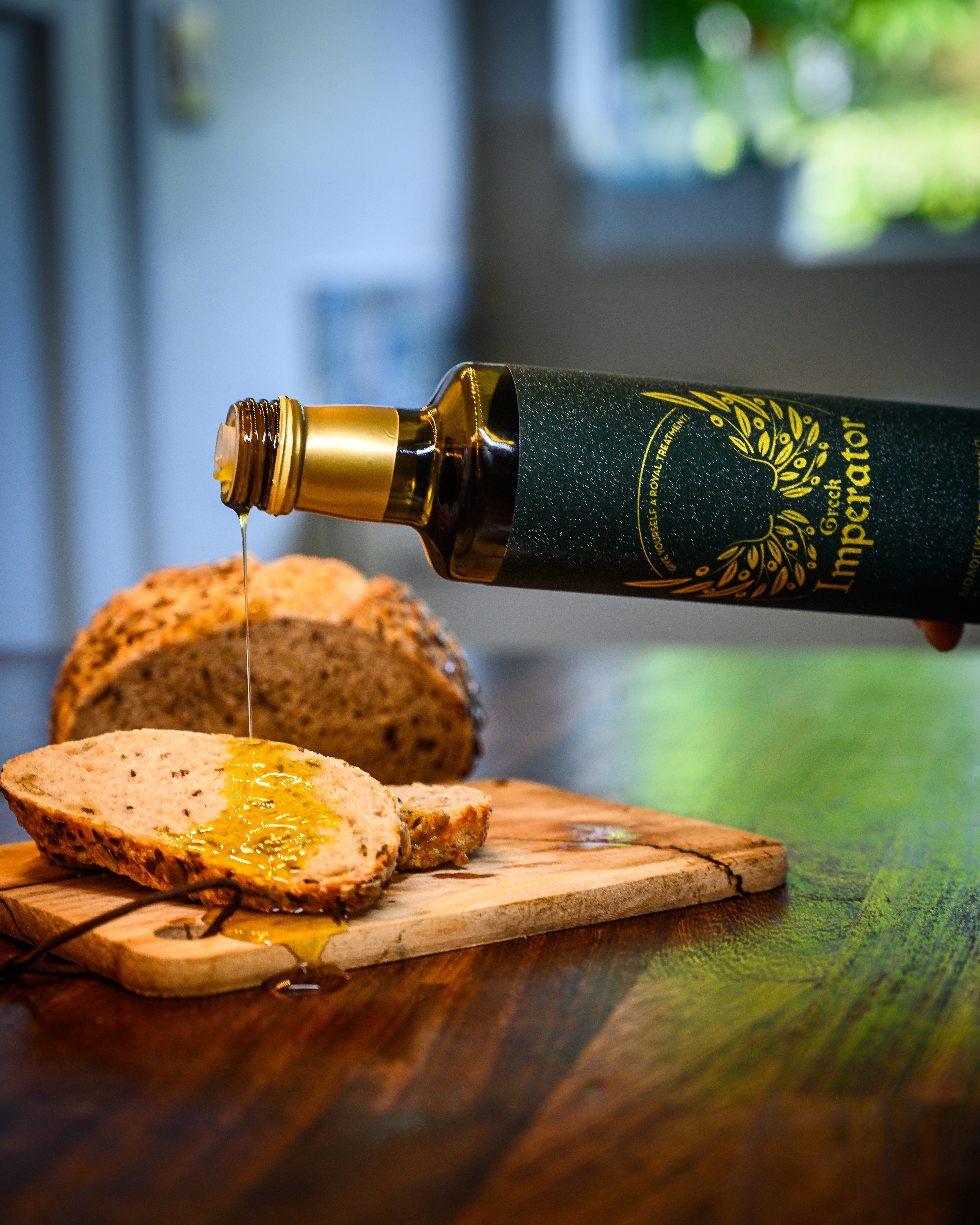Bottle of olive oil being poured onto bread on a wooden board with a blurred background