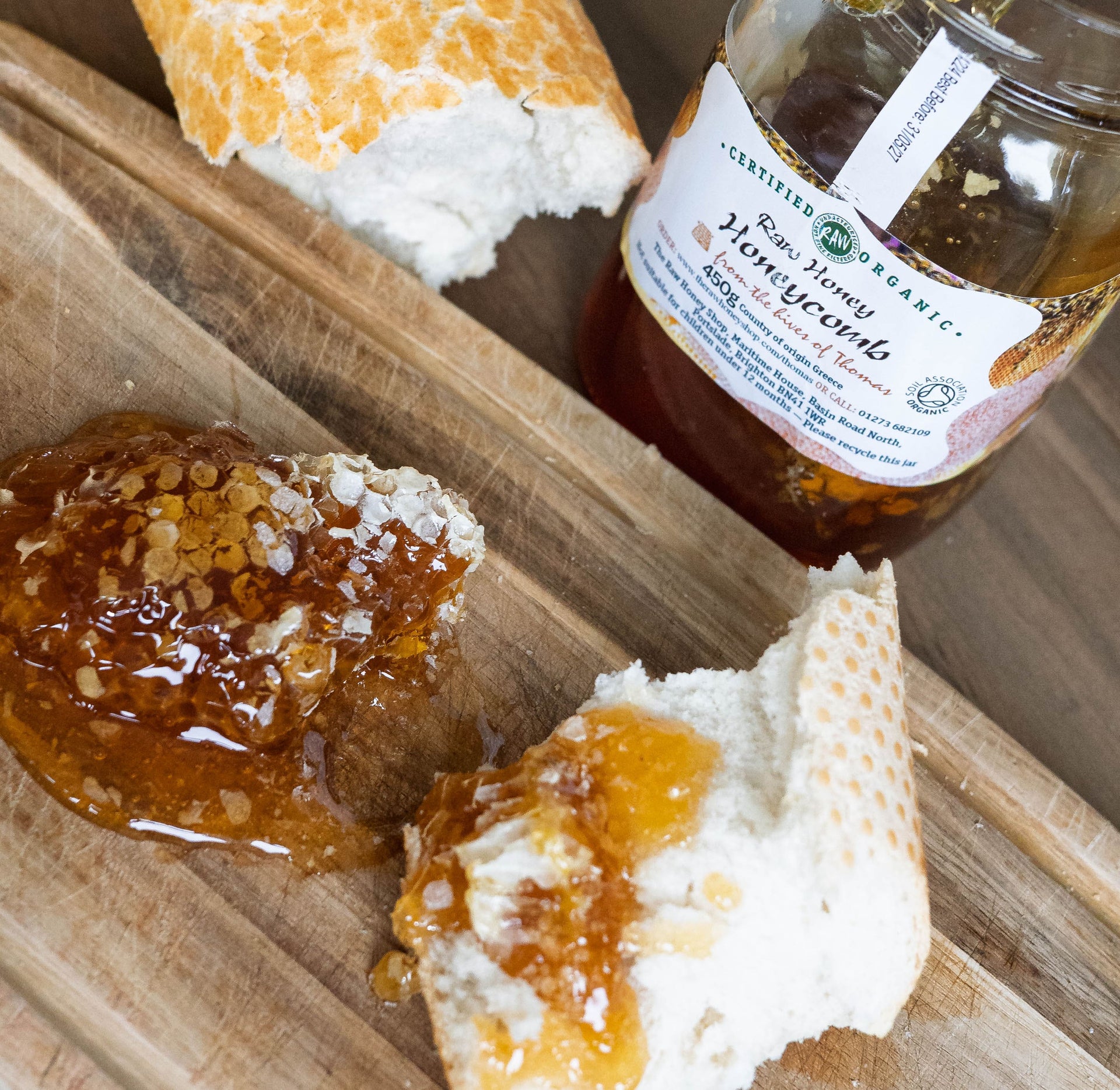 Jar of honeycomb with honey in the background.  White bread and honeycomb on a wooden board in the foreground.