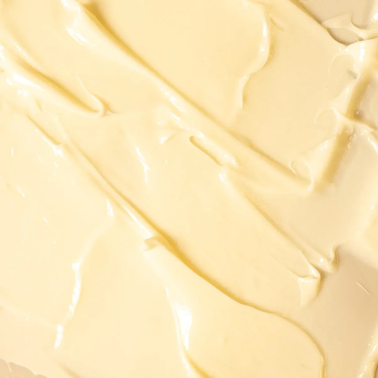 A close-up texture shot of a thick, creamy, pale yellow whipped substance with smooth, glossy swirled strokes.