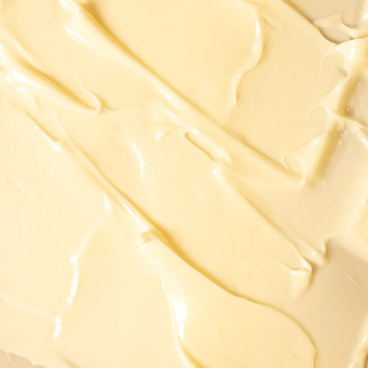 A close-up texture shot of a thick, creamy, pale yellow whipped substance with smooth, glossy swirled strokes.