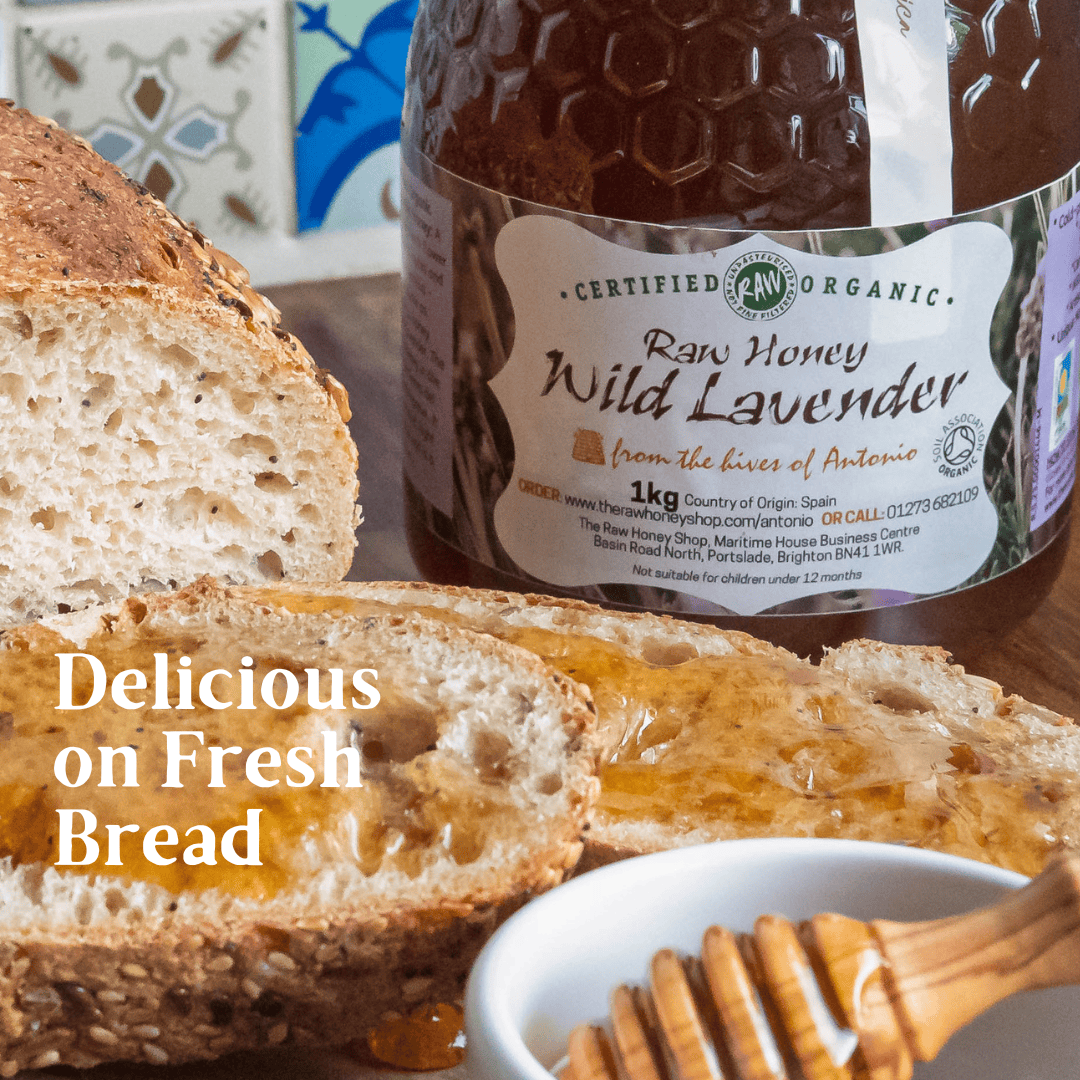 A jar of Certified Raw Organic Wild Lavender honey displayed next to slices of rustic bread spread with honey, with a wooden honey dipper in a small white bowl and the text 'Delicious on Fresh Bread'.