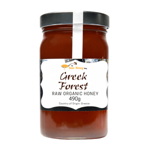A jar of Greek Forest Raw Organic Honey from The Raw Honey Shop, featuring a black lid, a white seal, and a white label with black text, set against a plain white background.