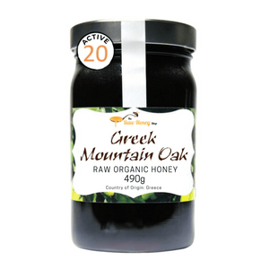 A jar of Greek Mountain Oak Raw Organic Honey from The Raw Honey Shop featuring a black lid, a white and green label, and an 'ACTIVE 20' seal on the upper left, set against a plain white background.