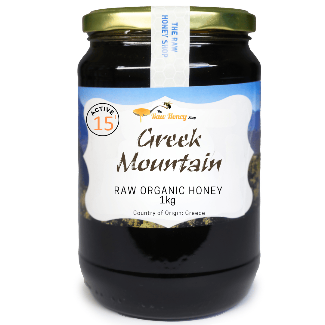 A 1kg glass jar of Greek Mountain Raw Organic Honey by The Active 15th and The Raw Honey Shop, featuring a white label with blue accents and a gold metal lid, set against a plain white background.