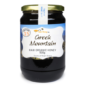 A 500g glass jar of Greek Mountain Raw Organic Honey with a gold metal lid and a white label, set against a plain white background.