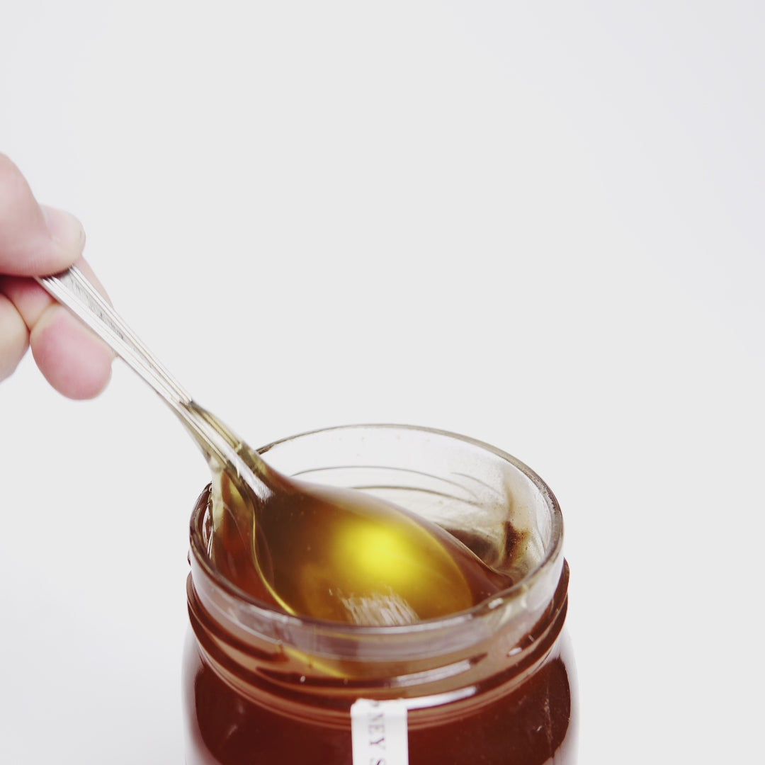 video of metal spoon dripping into an open jar of raw organic vanilla fir honey.