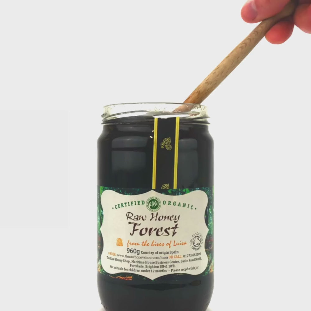 video of wooden honey dipper pouring into an open jar of raw organic forest honey.
