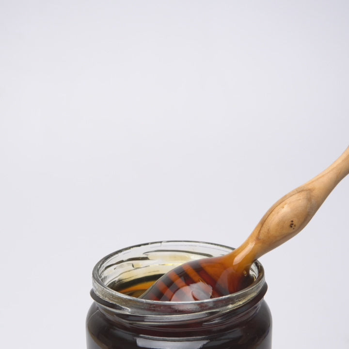 video of wooden honey dipper  dripping into an open jar of organic oak honey