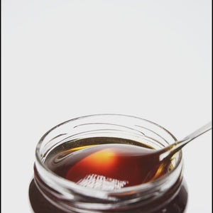 metal spoon of spring pine honey pouring into open glass honey jar