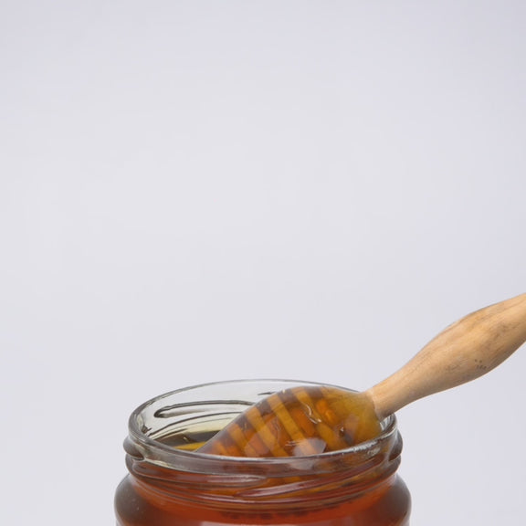 video of wooden honey dipper pouring into an open jar of  raw organic thyme honey