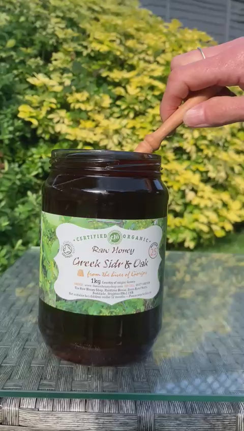 Jar of Greek Sidr and Oak honey being poured from a jar with a wooden honey dipper