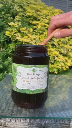 Jar of Greek Sidr and Oak honey being poured from a jar with a wooden honey dipper