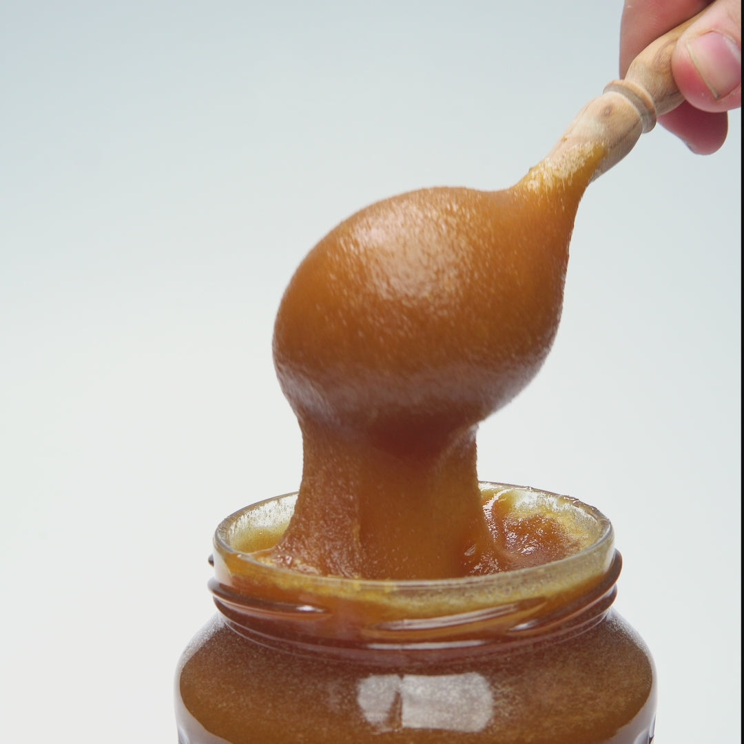 Video showing organic Buckwheat honey being pouring from a jar with a wooden honey dipper