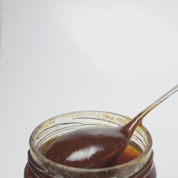 video of wooden honey dipper  dripping into an open jar of raw organic bell heather and mountain calluna honey