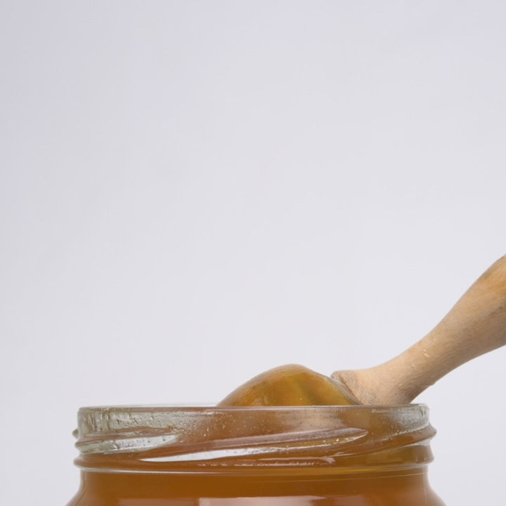 video of wooden honey dipper  dripping into an open jar of organic wild lavender honey