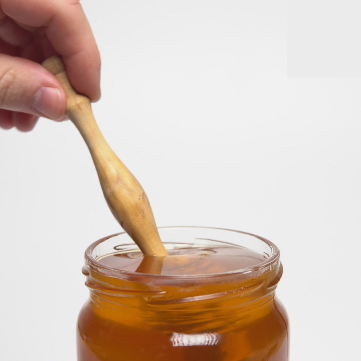 video of wooden honey dipper  dripping into an open jar of organic rosemary honey